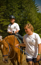 A counselor leads a camper's horse.